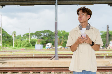 Young non binary tourist traveler in train station using phone