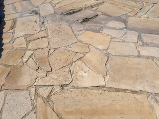 Close-up of irregular stone pavement surface with natural textured pattern, cracked shapes and grout lines, ideal for background, texture or architectural reference