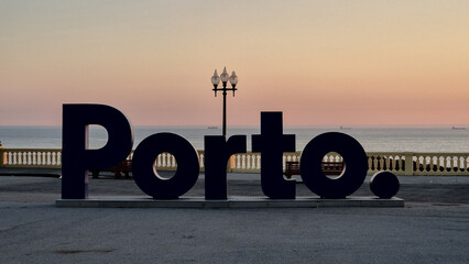 Sunset at Foz do Douro, Porto, Portugal. A silhouette of the iconic “Porto.” sign stands by the Atlantic, with pastel skies, distant ships, and calm waters marking the end of the day.
