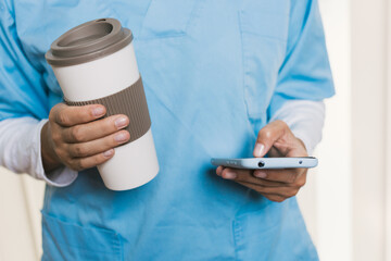 Nurse using smartphone and holding coffee mug during break time