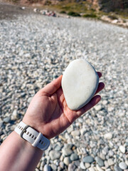 Smooth pebble beach with natural stones and people relaxing by the sea on a sunny day, showing textures of round rocks, hand holding stone and coastal landscape © Katarzyna Ledwoń