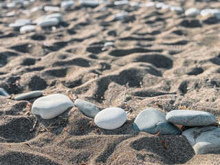 Smooth pebble beach with natural stones and people relaxing by the sea on a sunny day, showing textures of round rocks, hand holding stone and coastal landscape