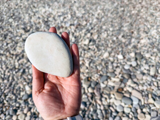Smooth pebble beach with natural stones and people relaxing by the sea on a sunny day, showing textures of round rocks, hand holding stone and coastal landscape