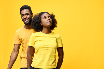 Cheerful young Black couple wearing matching yellow shirts, enjoying playful moments against a...