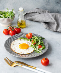 Fried eggs with arugula and cherry tomatoes on a dark plate on a blue txtured background