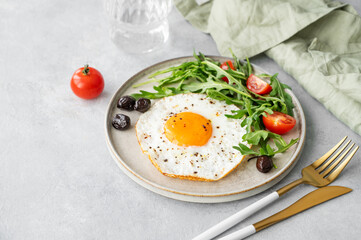 Fried eggs with arugula, ovives  and cherry tomatoes on a plate on a light background