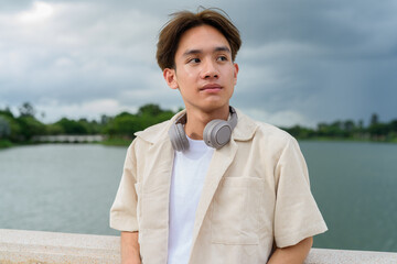 Asian non binary tourist person with headphones relaxing at park near lake