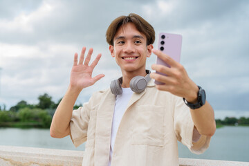 Asian non binary tourist person with headphones relaxing at park near lake using mobile phone