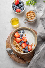 Natural yogurt with granola, blueberry and strawberry in a bowl on a wooden board on a light background