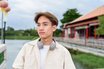 Asian non binary tourist person with headphones relaxing at park near lake