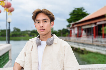 Asian non binary tourist person with headphones relaxing at park near lake