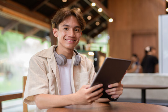 Handsome young non binary man sitting in cafe restaurant using digital tablet computer