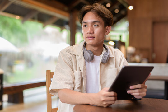 Handsome young non binary man sitting in cafe restaurant using digital tablet computer