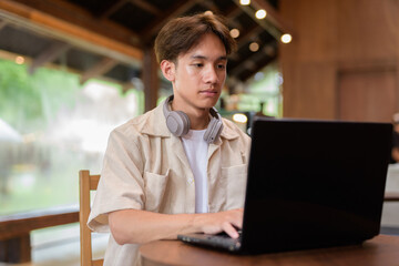 Handsome young non binary man sitting in cafe restaurant using laptop computer