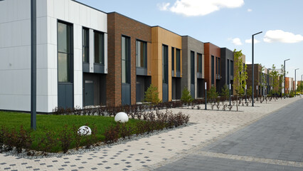 Modern residential street with row of stylish townhouses with varied architectural facades and manicured landscaping. Contemporary design new urban development and comfortable living spaces. 