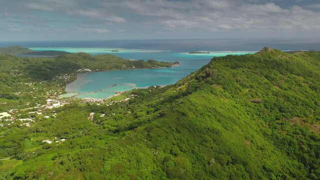 Tropical vegetation covers the mountain slopes of Bora Bora, a volcanic island in French Polynesia, while turquoise waters lap against the sandy shores of the lagoon
