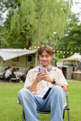 Young non binary person having road trip and camping with friends in nature using phone