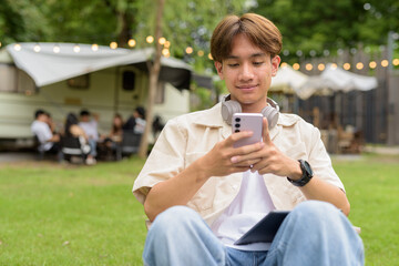 Young non binary person having road trip and camping with friends in nature using phone