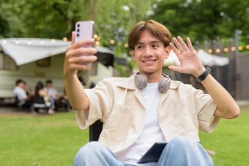 Young non binary person having road trip and camping with friends in nature using phone