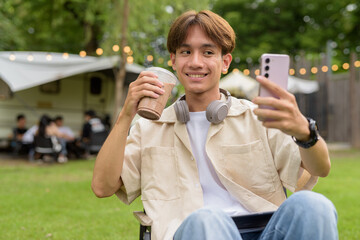 Young non binary person having road trip and camping with friends in nature taking selfie photo...