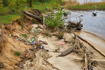 Pollution on a riverbank with plastic waste and driftwood.