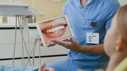 Close up of unrecognizable male dentist holding digital tablet with before and after on screen and explaining teeth whitening - Powered by Adobe