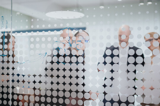 A group of business people engaging in a collaborative discussion during a meeting, writing on a glass surface adorned with decorative circles, emphasizing teamwork and communication.