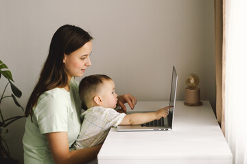 Portrait of happy young mother with little baby using laptop at home. Together, smiling mom...