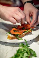 Chef hands preparing salmon sandwich with arugula and cream cheese