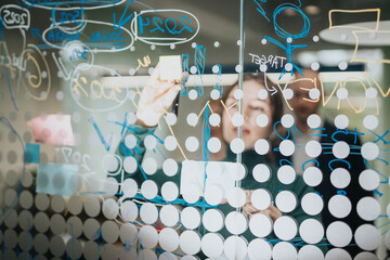 Diverse coworkers brainstorming, collaborating, and writing concepts on a transparent board,...
