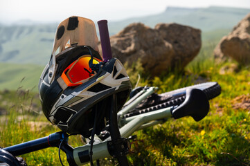 Close-up Mountain bike with helmet and mask lying on grass high in mountains against mountain...