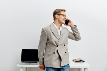 smiling man talking smartphone modern gray jacket casual jeans standing near laptop desk business...