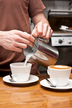 barista pouring milk into ceramic cups