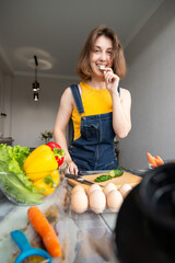 Cooking concept. Young woman in denim overalls preparing healthy dinner, vertical shot, smiling...