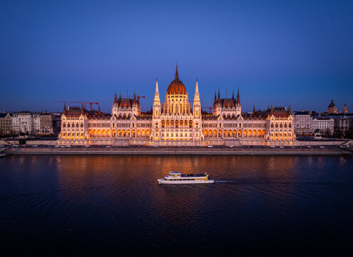 Aerial view of the illuminated Hungarian Parliament Building reflected in the tranquil waters of the Danube River, its ornate architecture glowing against the twilight sky, Budapest, Hungary.