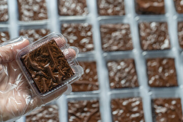 Hand Holding Fuggy Brownie on the right side Packaged Brownie in Production Line