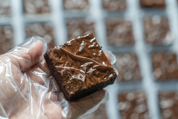 Gloved Hand Holding Packaged Brownie with Production Background