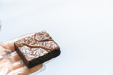 Close-up Gloved Hand Holding Brownie in Foreground left site, White Background