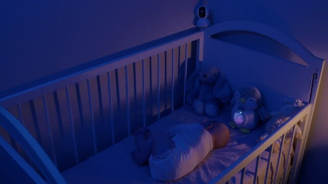 Infant baby sleeps with monitor and penguin lamp in cot