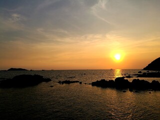 Obraz premium Golden tropical sunset over rocky sea coast in Thailand, peaceful scenic seascape for relaxation and meditation