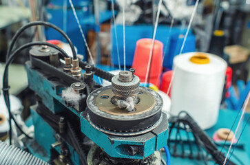 Textile industry, automatic knitting of socks. Circular knitting machine, colored threads on spools.