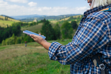 A close-up of a hiker's hands holding a smartphone, tracking a digital route marked by a dotted...