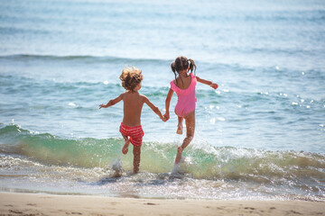 Activity on the beach in summer. Happy little girl with little boy jump into the sea. The kids in...