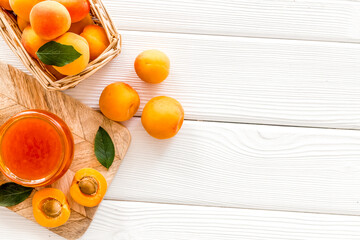 Summer preserves. Apricot jam in jar near fresh fruits on white wooden background top view frame...
