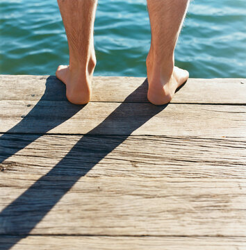 Detail of feet standing on wooden jetty with water in background