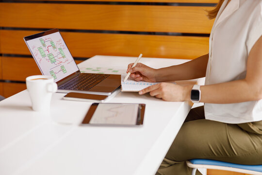 A professional woman skillfully writing notes as she works diligently on her laptop in a stylish office environment