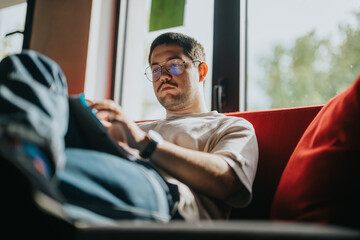 A young student focuses on studying at home, using a tablet while sitting comfortably on a couch...