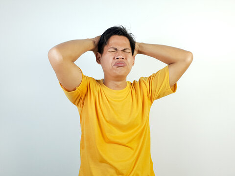 A young Asian man dressed in a yellow shirt, with a frustrated expression, holding his head in stress, portraying feelings of tension and difficulty.