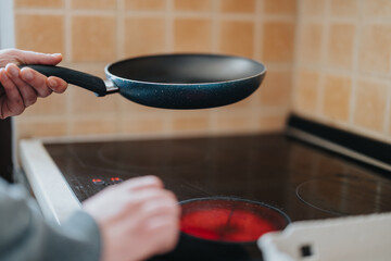 A close-up of a frying pan being held above a heated ceramic stove top burner with classic tiled...