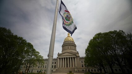 The West Virginia State Capitol stands proudly in Charleston, featuring impressive stone walls and a golden dome under a cloudy sky, attracting many visitors.